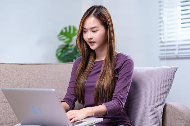 istock A young woman working on a laptop while sitting on a sofa, smiling and appearing focused, in a cozy home setting 2220056638