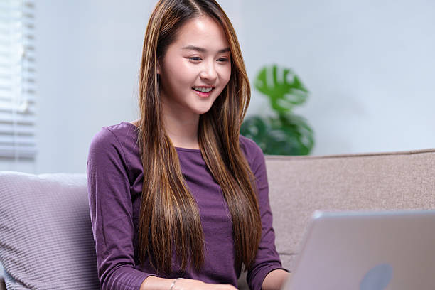 istock A young woman working on a laptop while sitting on a sofa, smiling and appearing focused, in a cozy home setting 2220056639