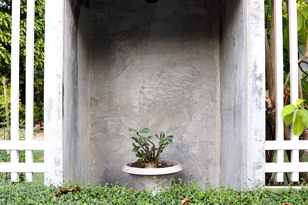 Big cement pot with flower plant in concrete frame between painted white metal fence.