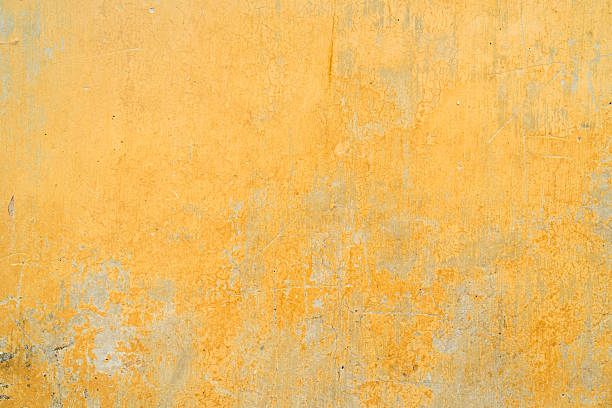 Close-up of an old yellow wall surface showing peeling paint, cracks, and weathered texture, ideal for background or design use.