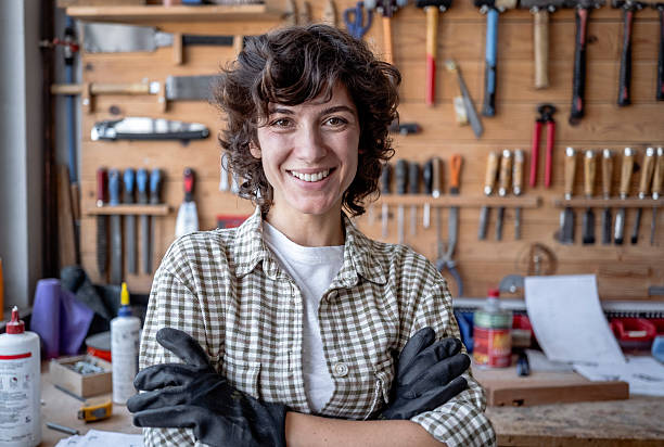 istock Confident Female Carpenter Smiling in a Workshop with Organized Tools and Wooden Background 2220074124