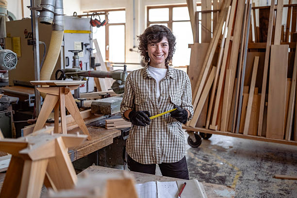 istock Young Female Carpenter in Bright Workshop Holding Measuring Tape Smiling Confidently 2220074133