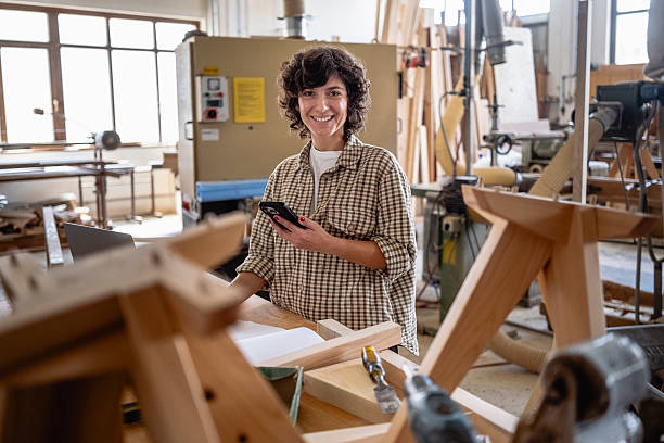 istock Smiling Female Carpenter in Checkered Shirt Working in Bright Woodworking Workshop 2220074134