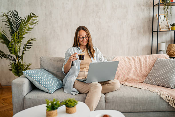 istock Young Woman Working On A Laptop And Drinking Coffee While Sitting On The Sofa At Home 2220074151
