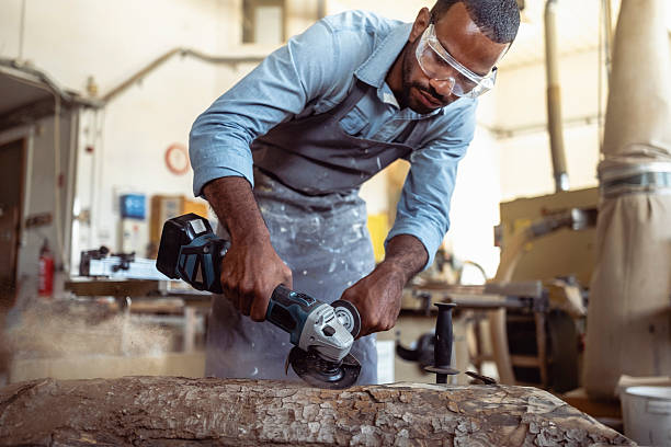 istock Skilled Craftsman Using Power Tool On Wooden Log In Industrial Workshop 2220074445