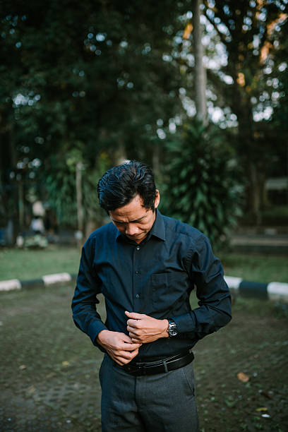 istock Formal asian man in park preparing for work attire buttoning shirt 2220076051