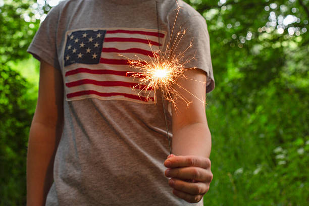 istock child with US flag holding lit sparkler. Celebrating US Independence Day 2220076170