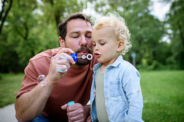 istock Father and son blowing soap bubbles in park. 2220076171