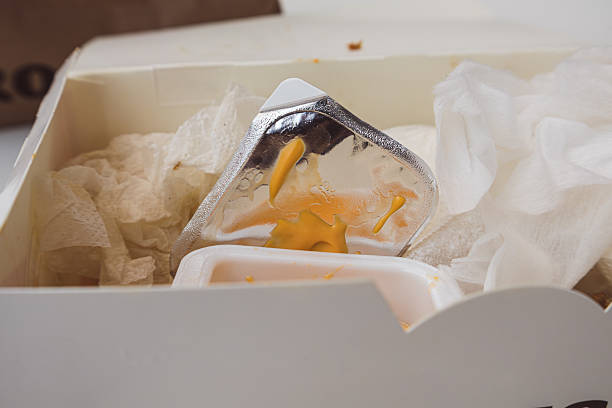 A cardboard food container with dirty napkins and leftover sauce in it