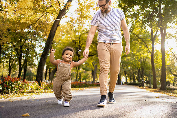 Father and his toddler joyfully walking hand in hand on a sunlit path in a park