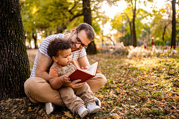 istock Father and son reading a book in the park during autumn 2220079009