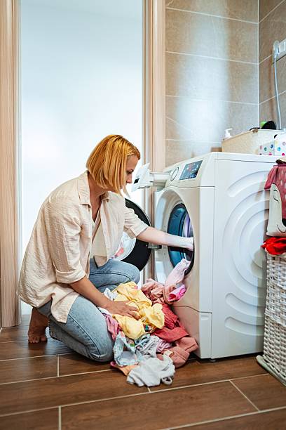 istock Woman loading clothes into washing machine in bathroom 2220079693