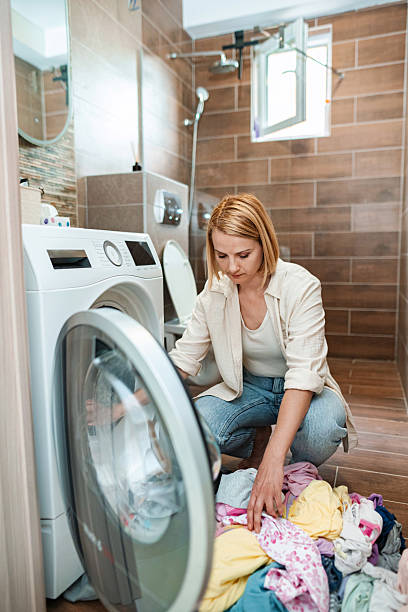 istock Woman putting clothes into washing machine in bathroom 2220079809