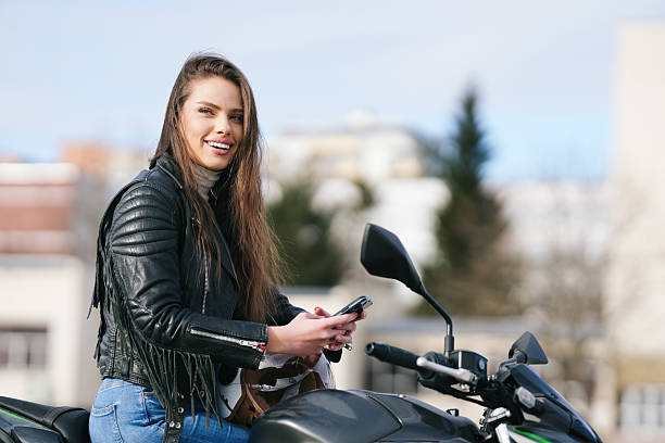 istock Smiling Woman on a Motorcycle While Checking Her Mobile Phone in a Trendy Setting 2220083806