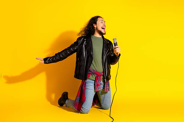 istock Young man with microphone in an energetic pose against vibrant yellow background expressing excitement and creativity 2220084766