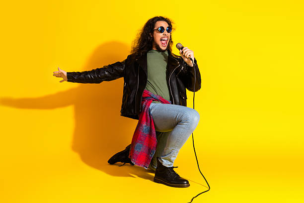 Young man in stylish casual attire performing with a microphone on a bright yellow backdrop, expressing joy and energy.