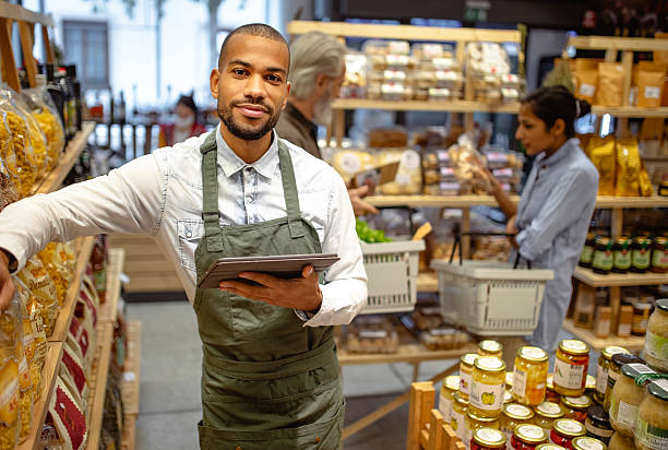 istock Confident Multiracial Male Grocery Worker in Green Apron Using Digital Tablet in Store 2220085584