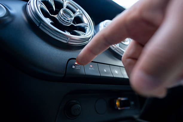 Close-up of a hand interacting with a car's dashboard air conditioner controls, focusing on comfort and technology. The image highlights the details of the automobile interior and depicts modern conveniences.
