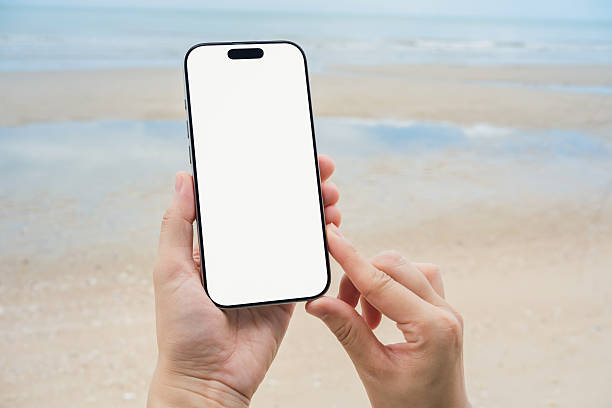 istock Hand holding a smartphone with a blank screen, on the sea and sandy beach background. Summer vacation concept. 2220089764