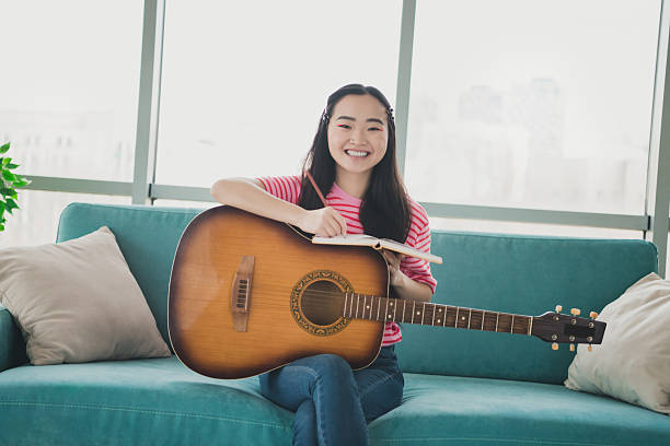 istock Young woman sitting on a couch with a guitar, smiling and writing notes in a journal during a peaceful indoor day 2220089848