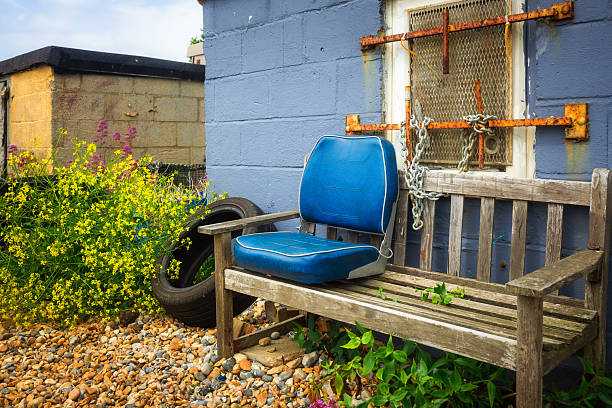 A deserted wooden bench, equipped with a blue cushion, stands alone on a pebble beach in southeast England.