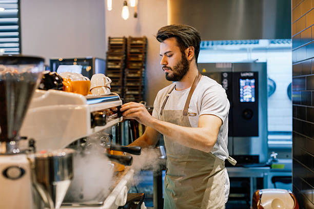 istock Young Male Barista Focused on Preparing Fresh Espresso Using a Professional Machine in a Trendy Coffee Shop 2220093052