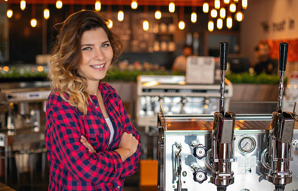 Smiling Young Female Barista in Plaid Shirt Posing by Professional Espresso Machine in Contemporary Coffee Shop