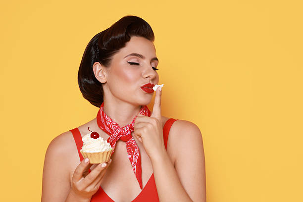 istock Pin-up woman eating cupcake on orange background, space for text 2220097207
