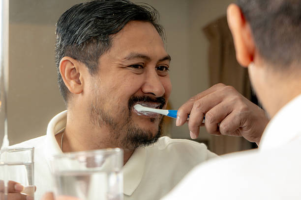 istock Young man brushing teeth in bathroom mirror at home 2220099027
