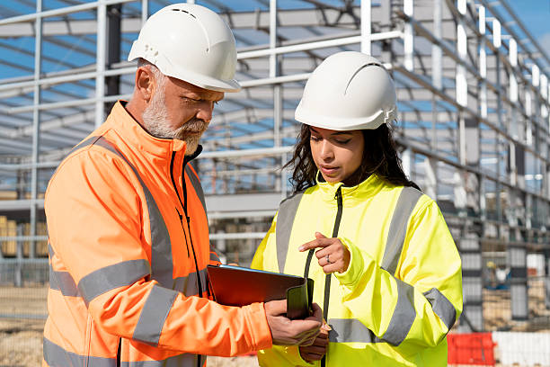 istock Two construction workers discuss plans on a site while wearing safety gear and reviewing documents 2220107952