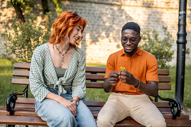 istock Two Friends Talking and Smiling on a Bench in a Park 2220116060