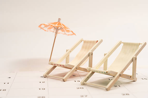 istock Two miniature beach chairs and a cocktail umbrella sit on a calendar page, symbolizing upcoming vacation plans 2220123027