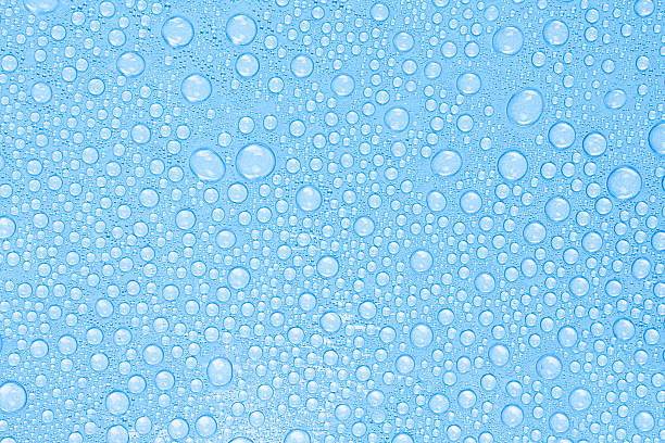 Macro image of transparent water drops on a smooth blue surface. The abstract pattern of droplets creates a natural, clean, and refreshing texture. Stock photo.