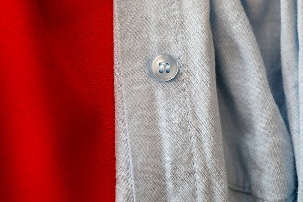 Blue shirt fabric with a single button in close-up, contrasting with a bright red background. This combination of colors and textures creates an interesting visual effect, highlighting clothing details.