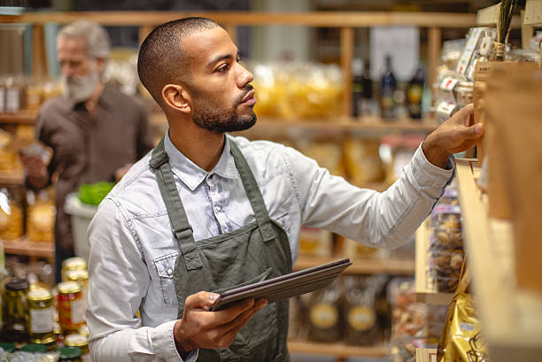 istock Focused Multiracial Grocery Worker Using Digital Tablet in Well-Lit Store Aisle 2220128516