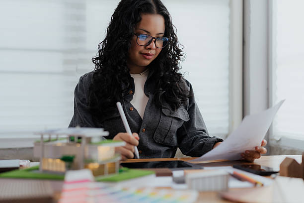 An intelligent female professional with glasses is focused on her research, analyzing project data on a tablet