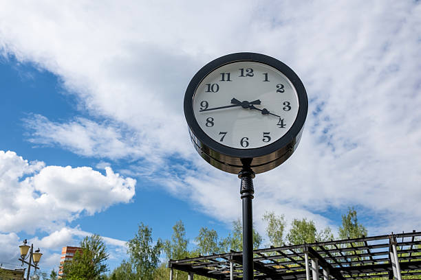 A decorative clock stands tall in a park surrounded by greenery, displaying the time around three oclock on a sunny afternoon.