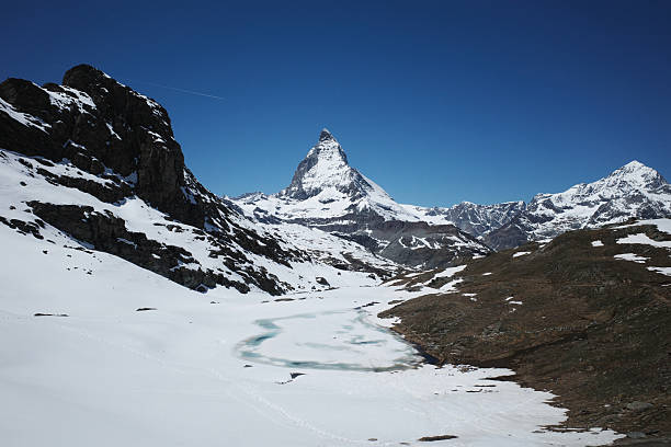 Zermatt, Switzerland. May 30, 2025. The pointy mountain peak against blue sky is the famous Matterhorn. The frozen lake is the Riffel lake.