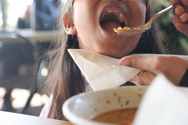 Young girl happily eating while someone assists her with a spoon.