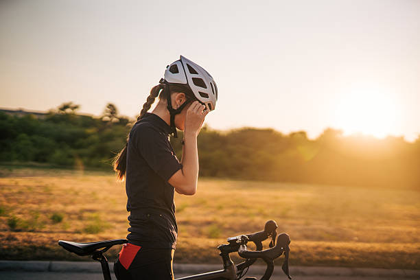 istock Young female cyclist putting on helmet at sunset 2220146004