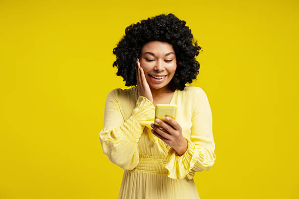 istock Curly African American woman using smartphone and looking at screen isolated on yellow background 2220149638