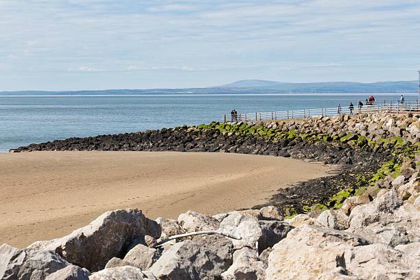 istock A sandy beach curves gently into the sea, bordered by rocky formations and a breakwater. 2220150284