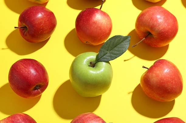 istock Green apple surrounded by red ones on yellow background, above view 2220151032