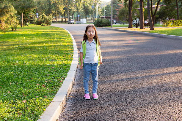 istock Young girl with backpack stands on sunny park path 2220154570
