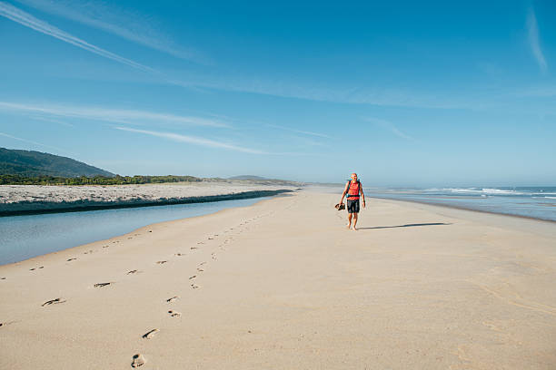 Lonely barefoot backpacker man walking by sandy Portugese beach in morning on the Atlantic ocean coast. Shot during the Camino Portuguese - popular pilgrimage route. Active people, traveling concept.