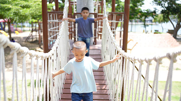 A two children playing on rope bridge in park, showcasing joy and adventure. scene captures essence of childhood exploration and friendship