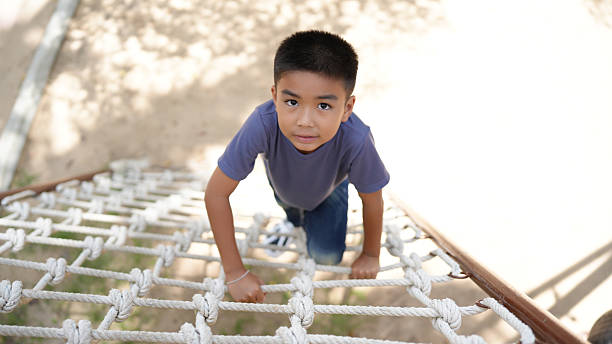 istock Young boy climbs rope ladder at playground, showcasing determination and focus. sunlight casts soft shadows, enhancing playful atmosphere of outdoor fun 2220157588