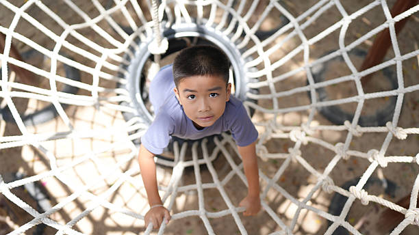 istock Young boy is climbing through rope net structure, showcasing determination and curiosity. scene captures joy of play and exploration in outdoor setting 2220157589