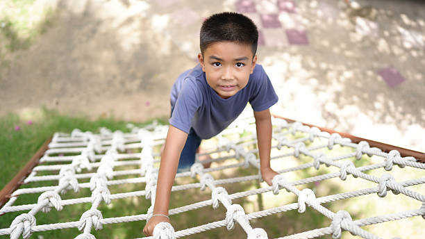 istock Young boy climbs on rope net, showcasing determination and playfulness. scene captures moment of adventure and exploration in natural outdoor setting 2220157612