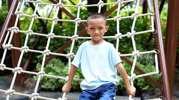 istock Cheerful child sits on rope climbing structure, smiling confidently. vibrant greenery in background adds lively touch to playful scene, capturing essence of childhood joy 2220157630